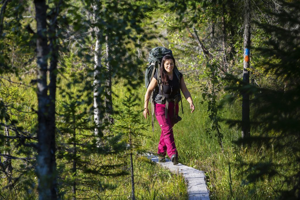 Nainen kävelee rinkka selässä pitkospuita pitkin.
