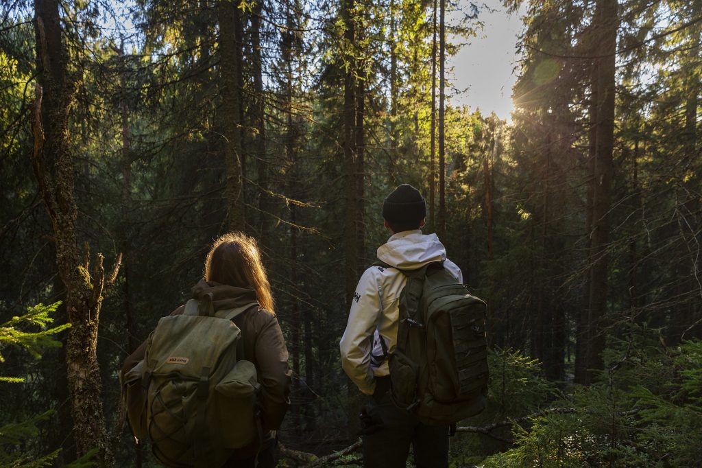 Nuori mies ja nainen katsovat metsämaisemaa selin kameraan.