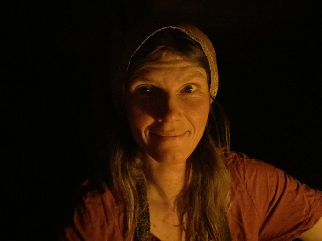 Nainen hymyilee ystävällisesti hämärässä ja katsoo suoraan kameraan.