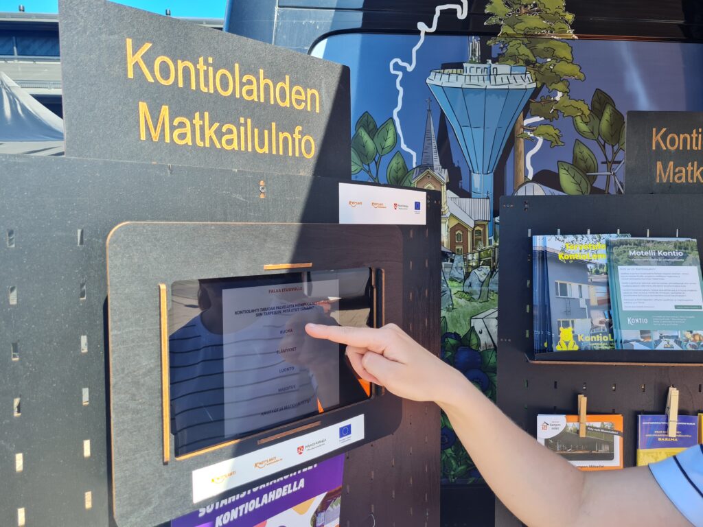 Kontiolahden MatkailuInfon tabletti, jonka näyttöä sormi on juuri painamaisillaan.